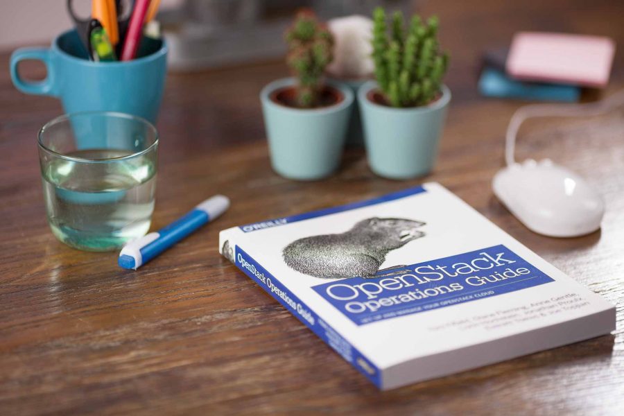 An OpenStack book on a desk surrounded by a glass of water, pencil and potted plants. Photo by Christian Demarcos
