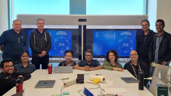 A group of 10 smiling people kneeling in front of a monitor showing the blue book cover