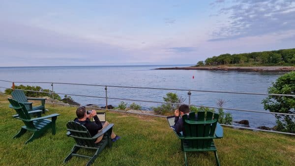 Two people sitting in lawn chairs with a view of the ocean, working on their laptops