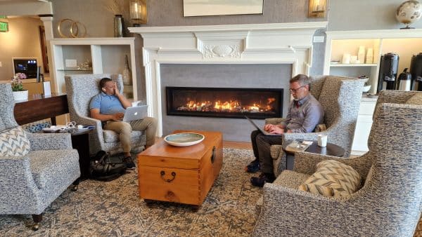 Two people sitting by a fireplace looking at their laptops deep in thought