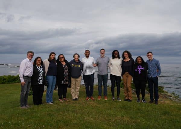 A group of eleven people standing on a lawn, in the background a cloudy sky and a view of the ocean.